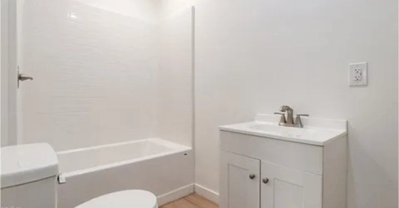 A simple, bright white bathroom with a white vanity sink, a bathtub with a shower surround, and a toilet.