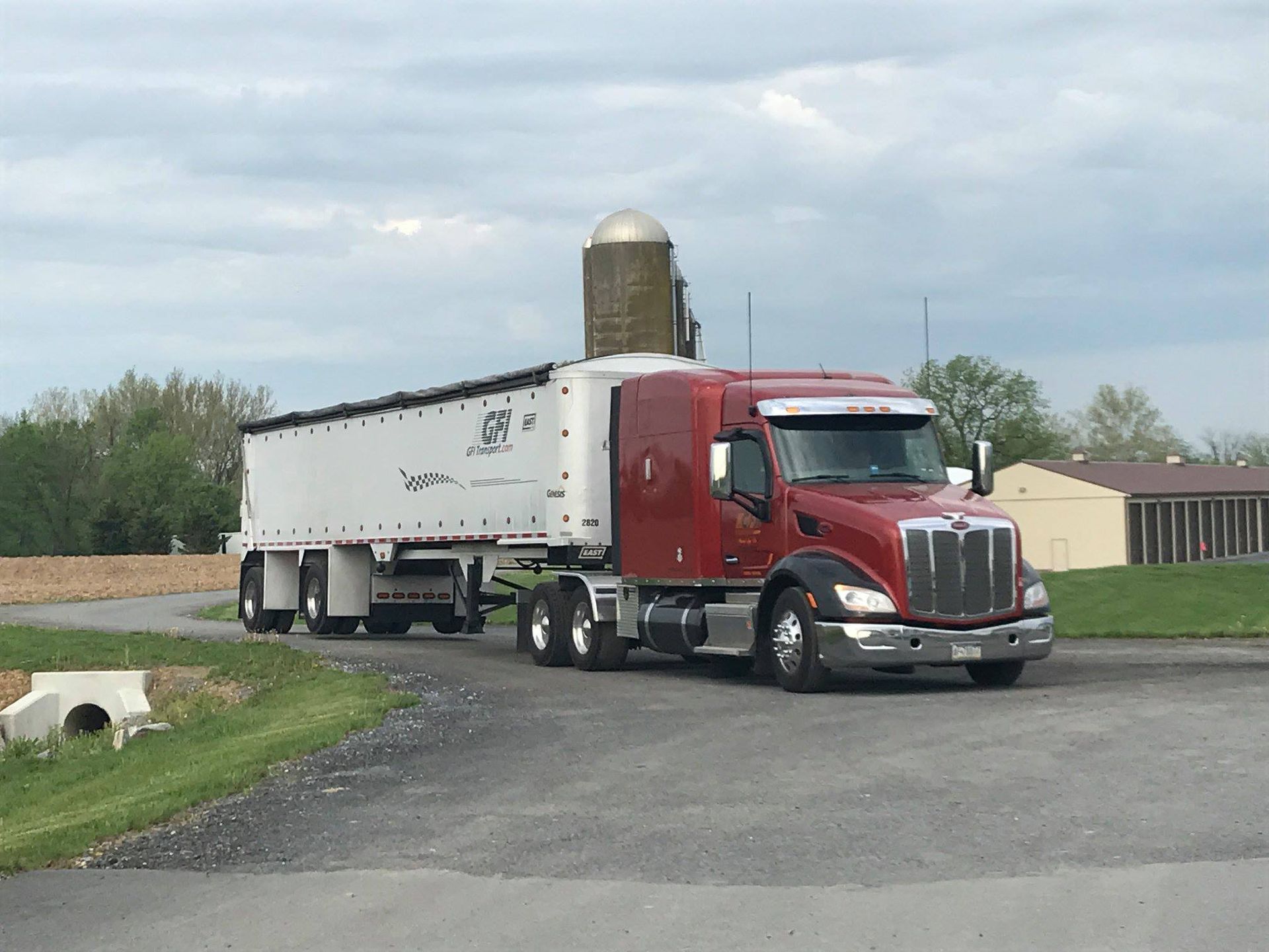 Red semi-truck with a white trailer on a road, near a silo.