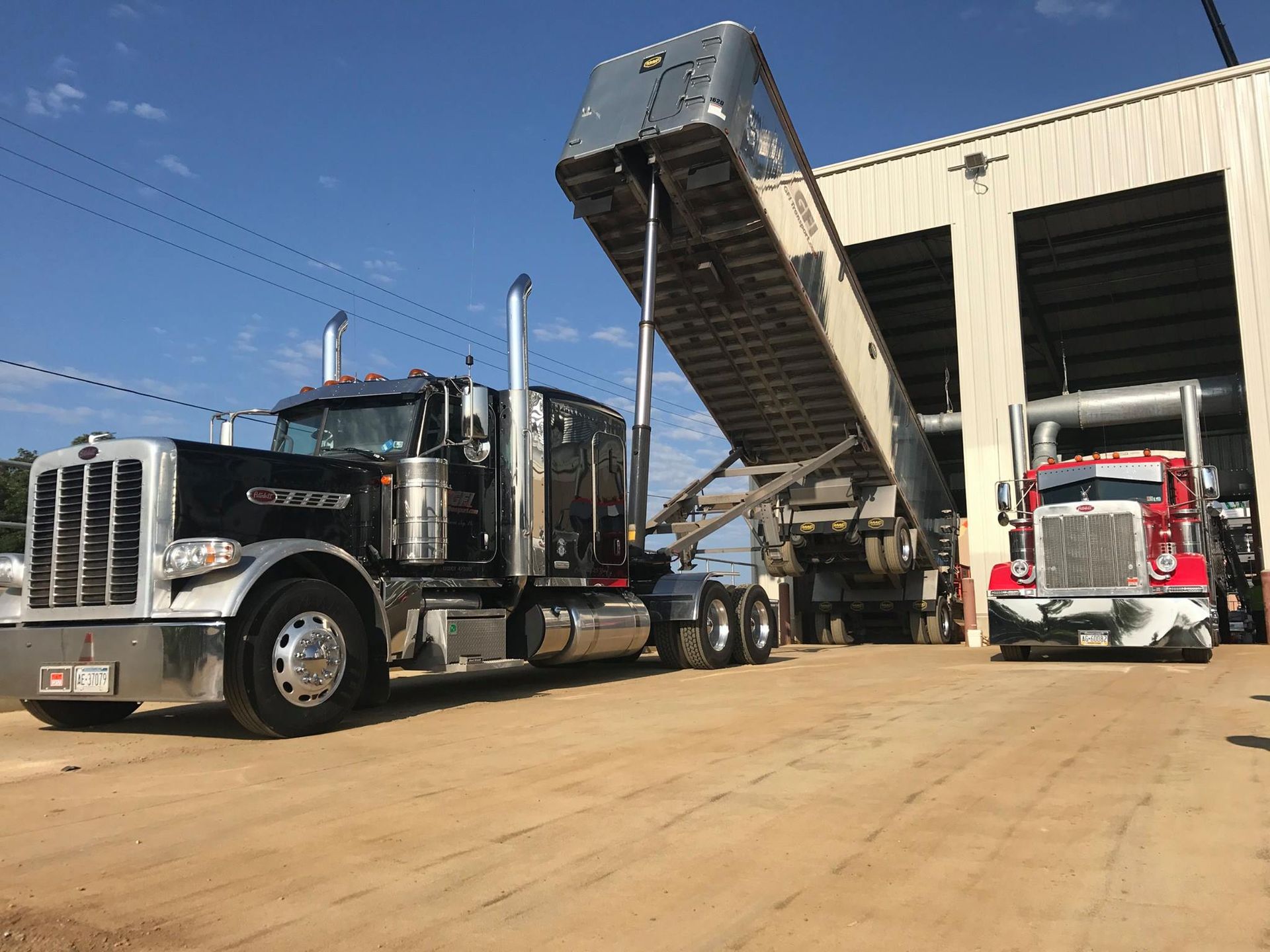 Black truck with raised dump bed unloading, next to a red truck in a building.