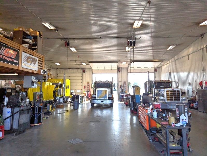 A bright, spacious mechanic garage with three large semi-trucks parked in individual bays.