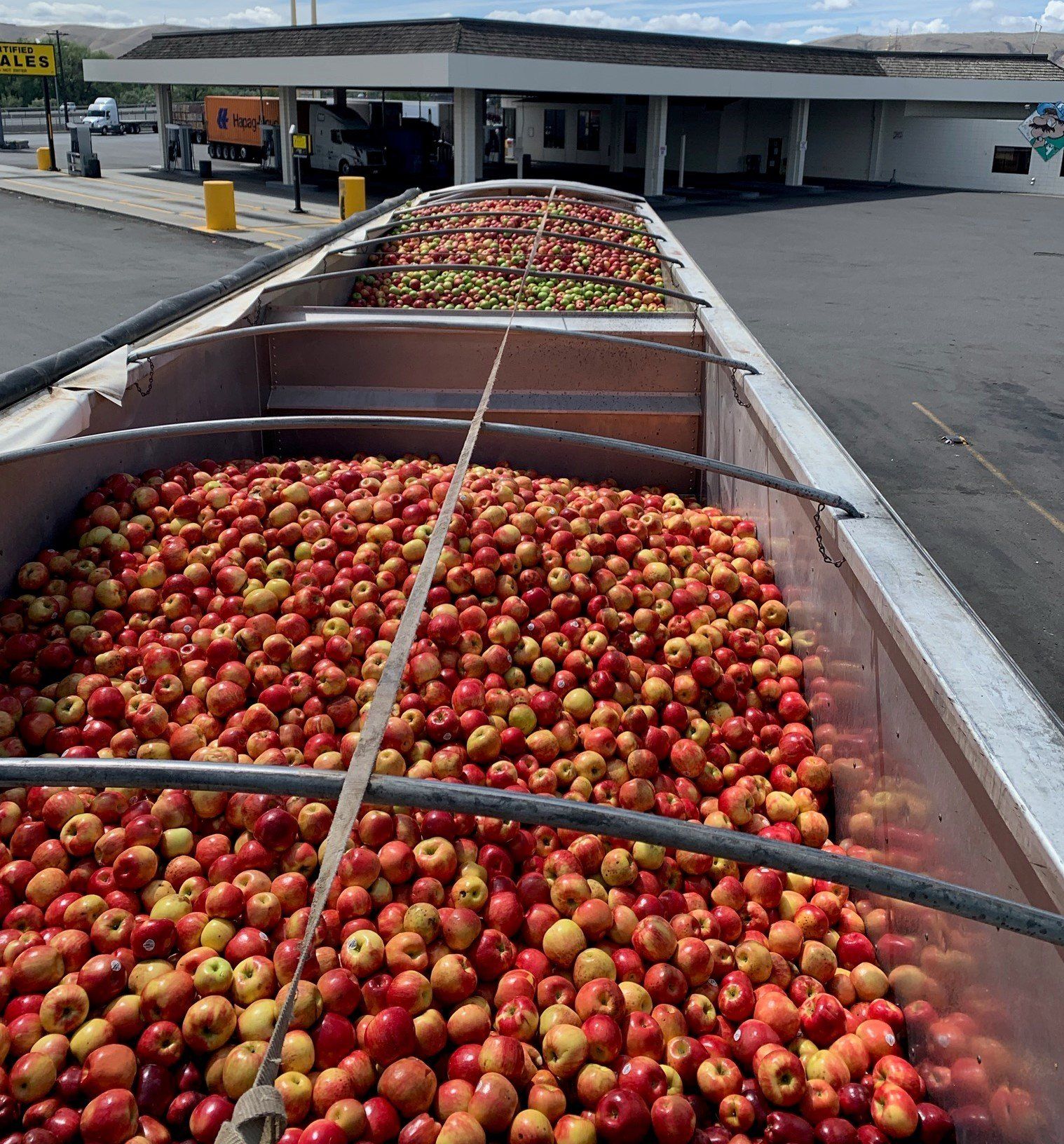 A truck full of apples is parked in front of a gas station from GFI Transport