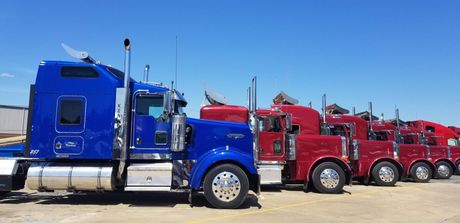 A row of semi trucks parked next to each other in a parking lot.