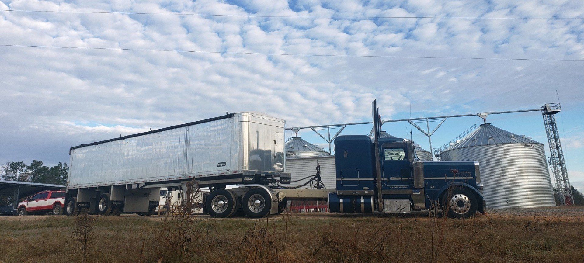 A semi truck is parked in a field with silos in the background.