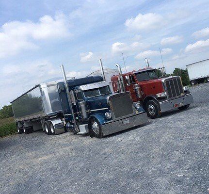 Two semi trucks are parked next to each other in a gravel lot.