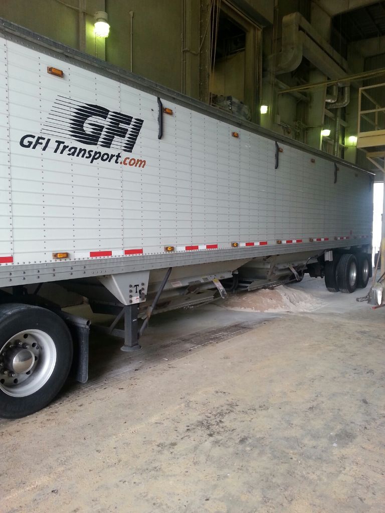 A red GFI Transport dump trailer semi truck is parked in front of a building.