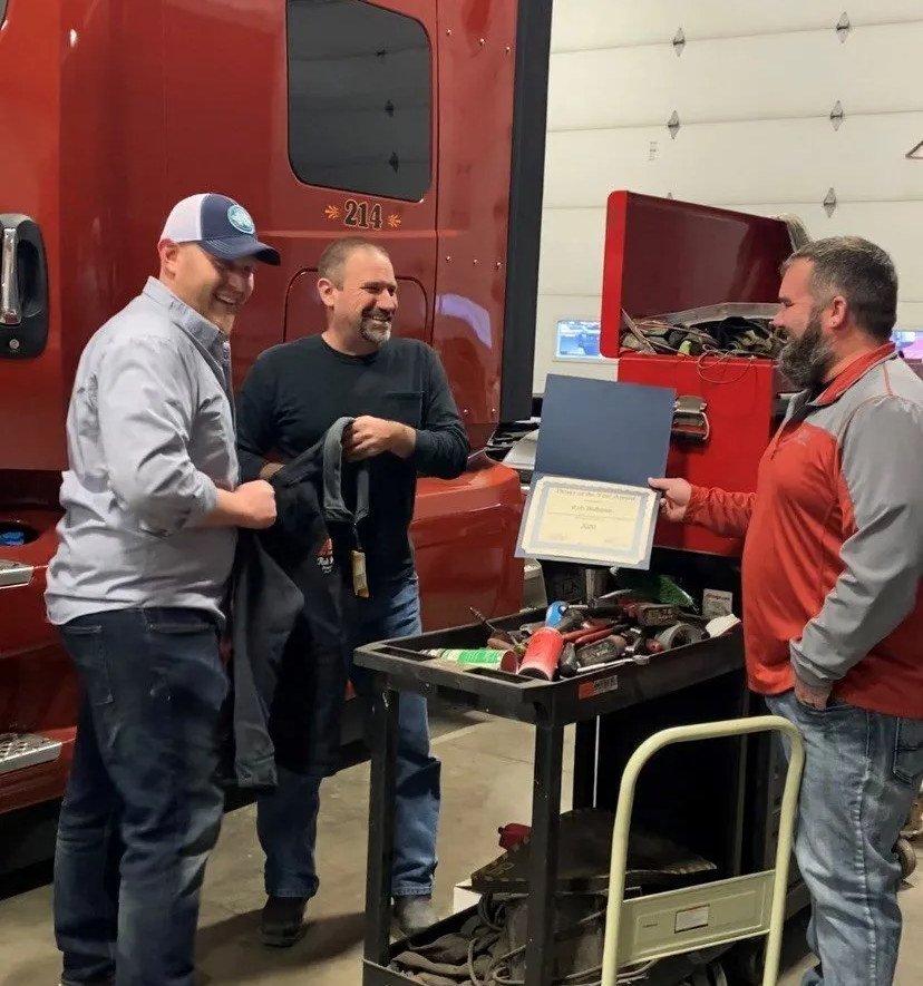 A group of men are standing in front of a red truck from GFI Transport