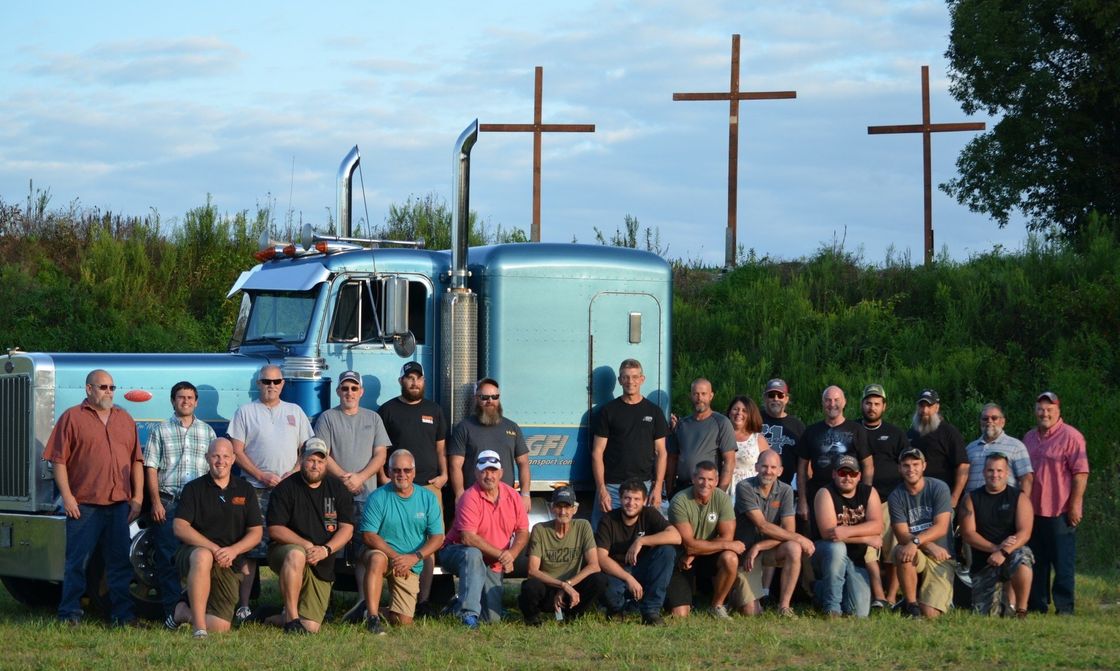 A group of people posing for a picture in front of a truck with three crosses in the background