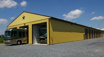 Two rvs are parked in front of a large yellow building.