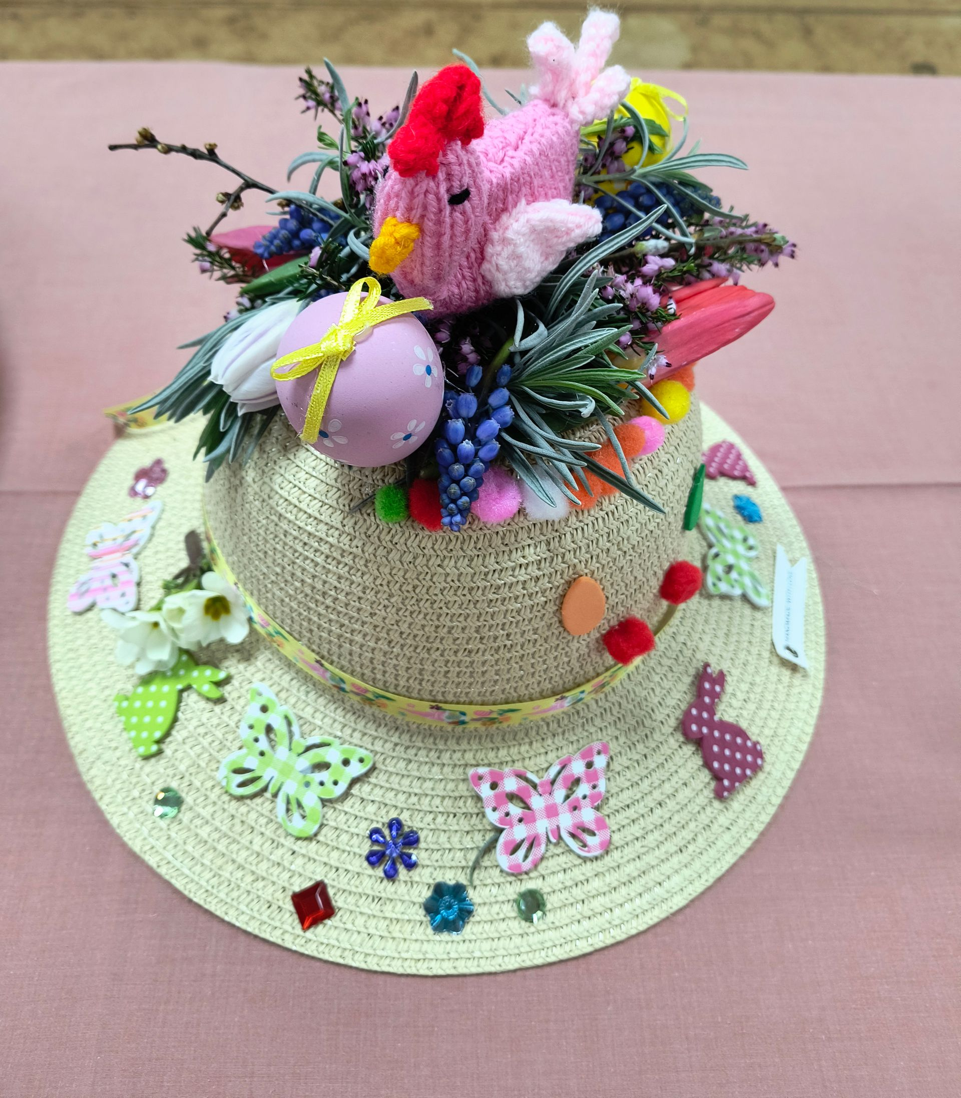 Photo shows a child's straw hat deocrated with plants, coloured eggs and a knitted chick