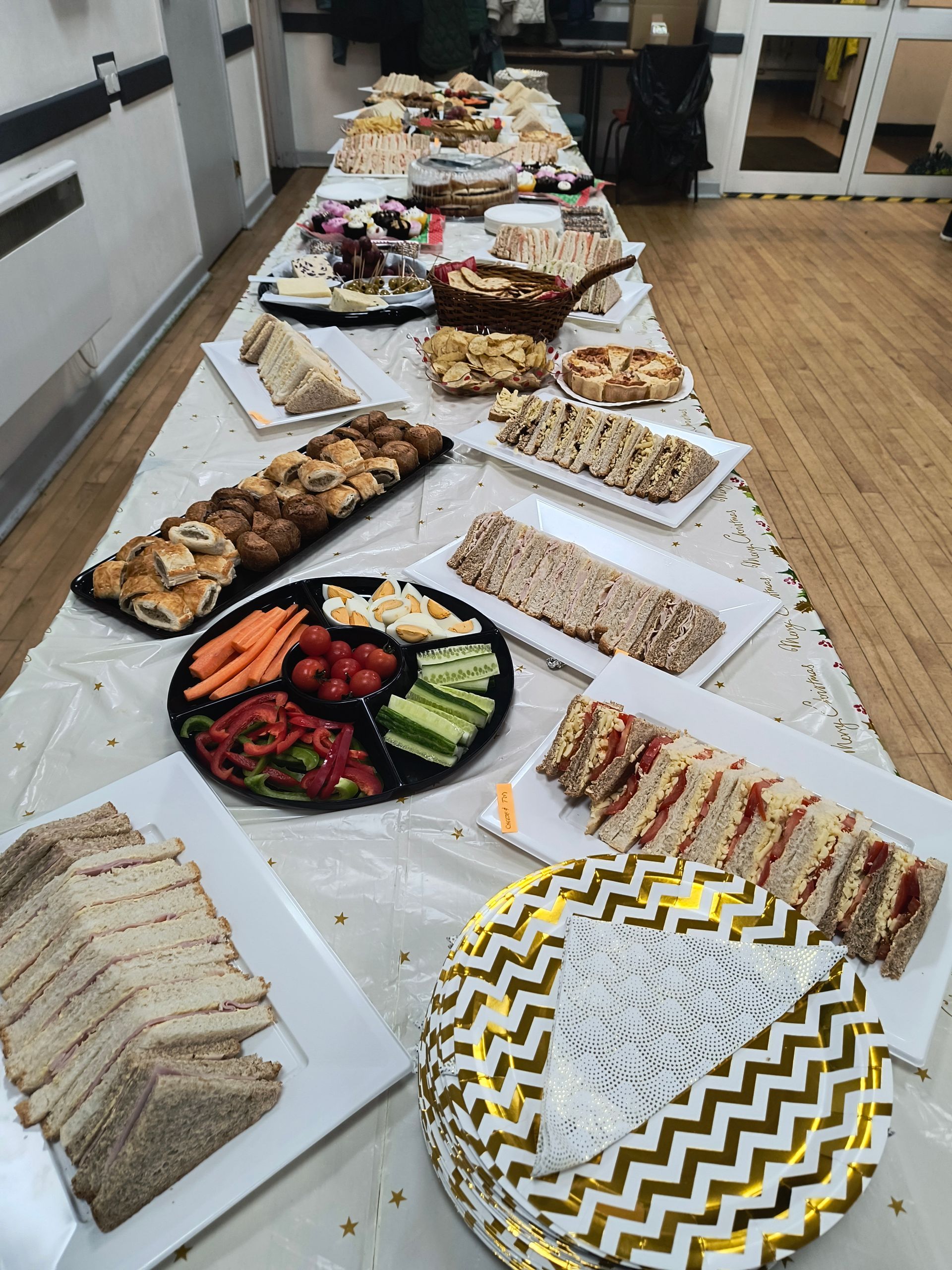 A buffet consisting of sandwiches, pastries, vegetables, boiled eggs, cakes and biscuits laid out on a long table