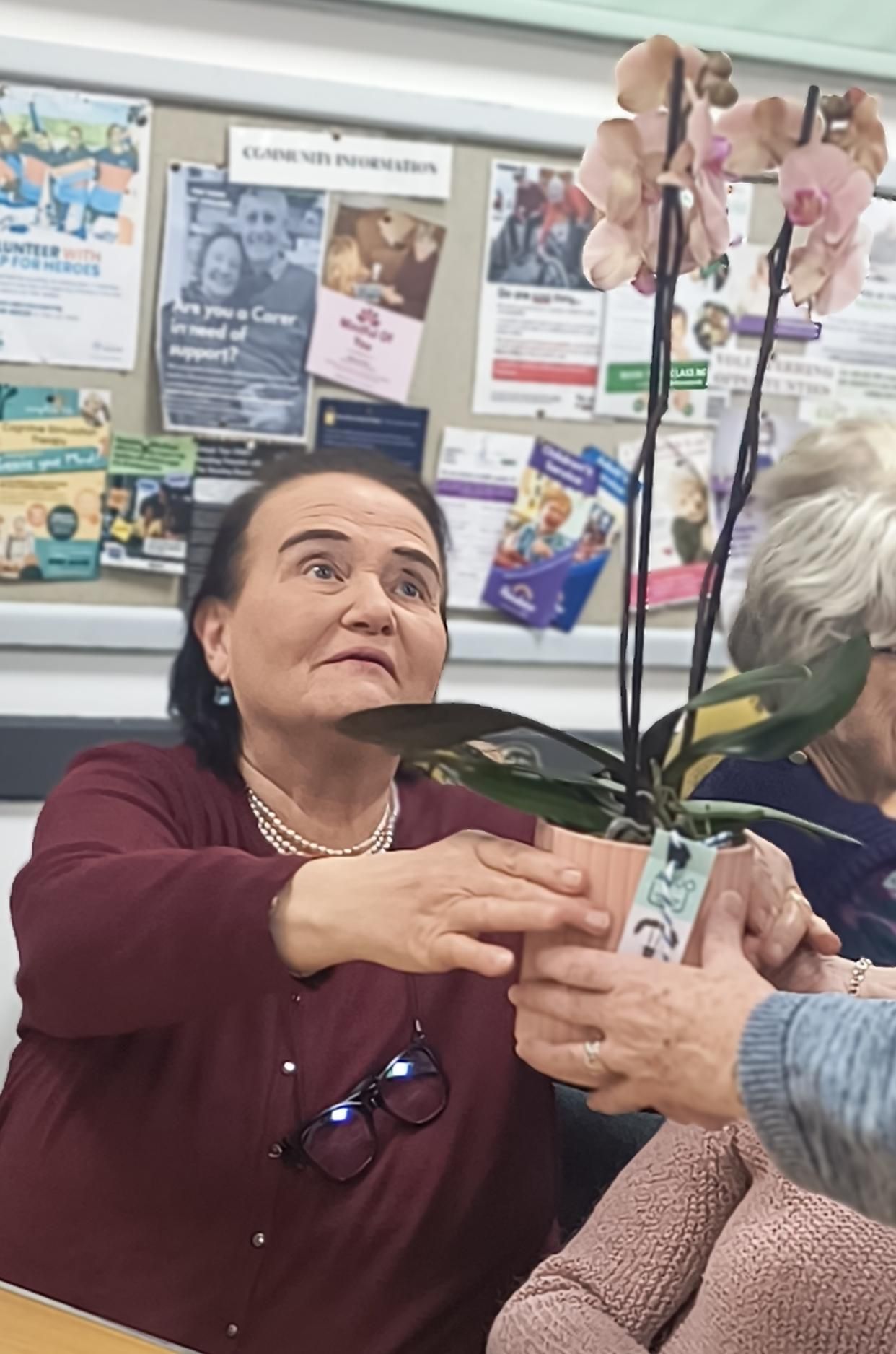 Theresa Duggan seated at a table accepts a pink potted orchid from another member whose hands are visible