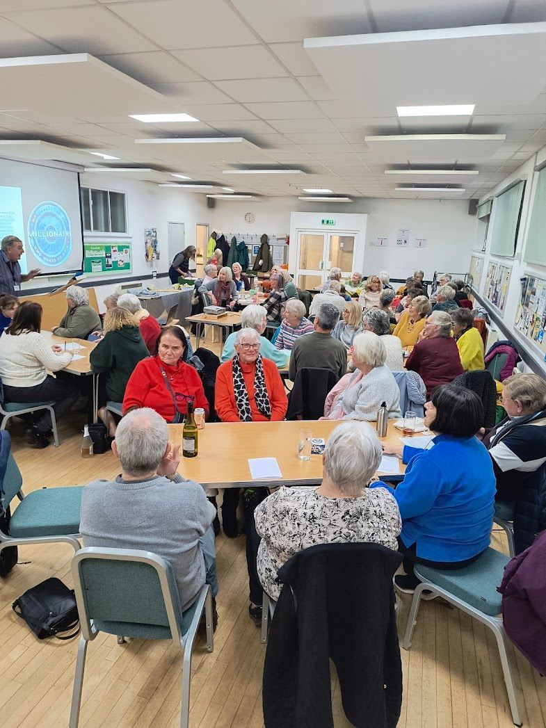 Photo shows people sitting at tables looking at a screen with a 