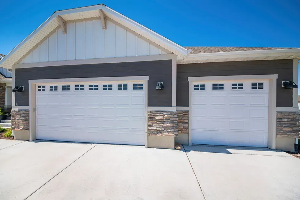 Home exterior with white double garage doors with windows and half stone walls