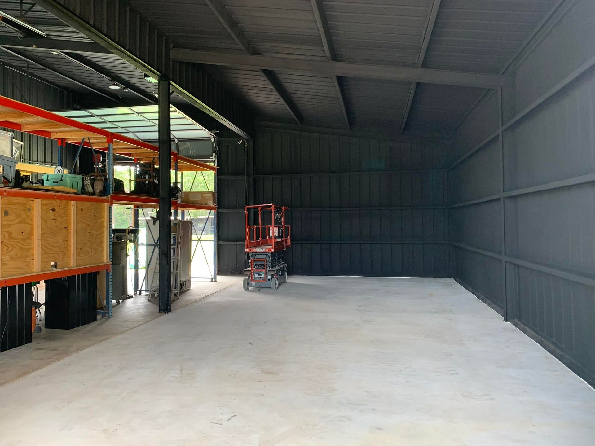 Interior of a large metal shed with a lift, storage shelves, and concrete floor. Walls are painted black.