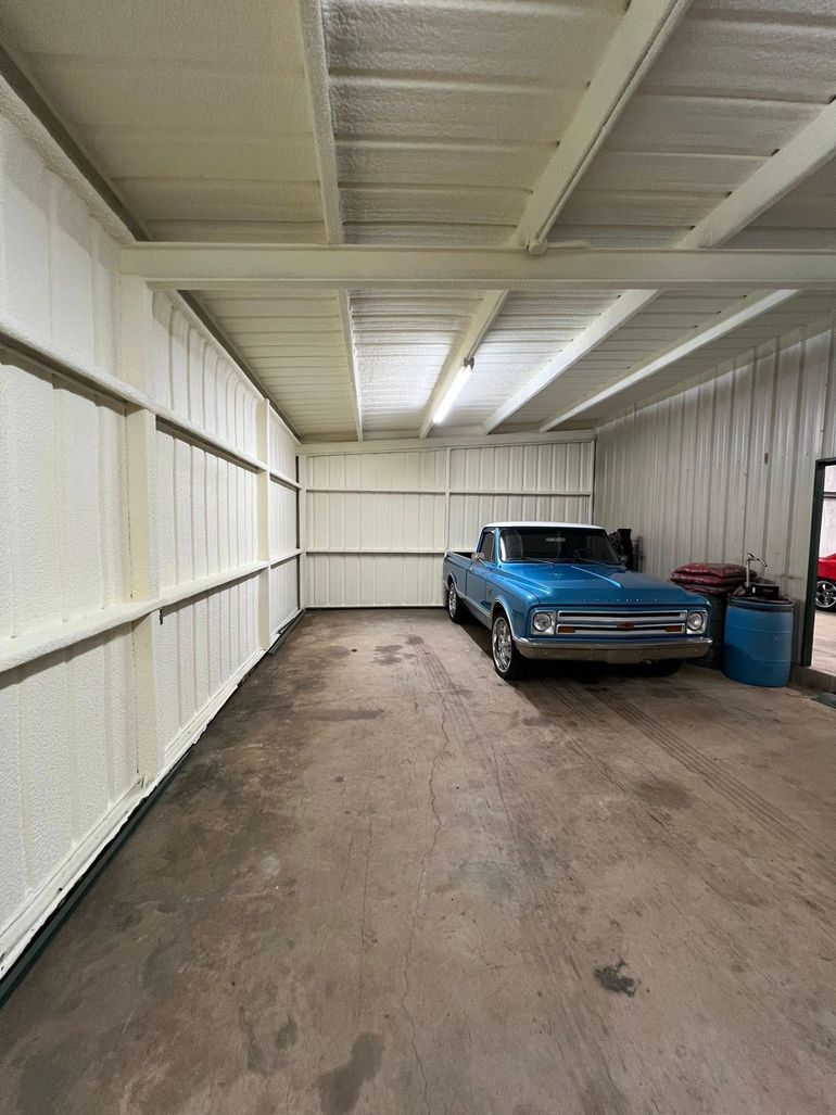 Blue pickup truck inside a garage with spray foam insulation on the walls and ceiling.