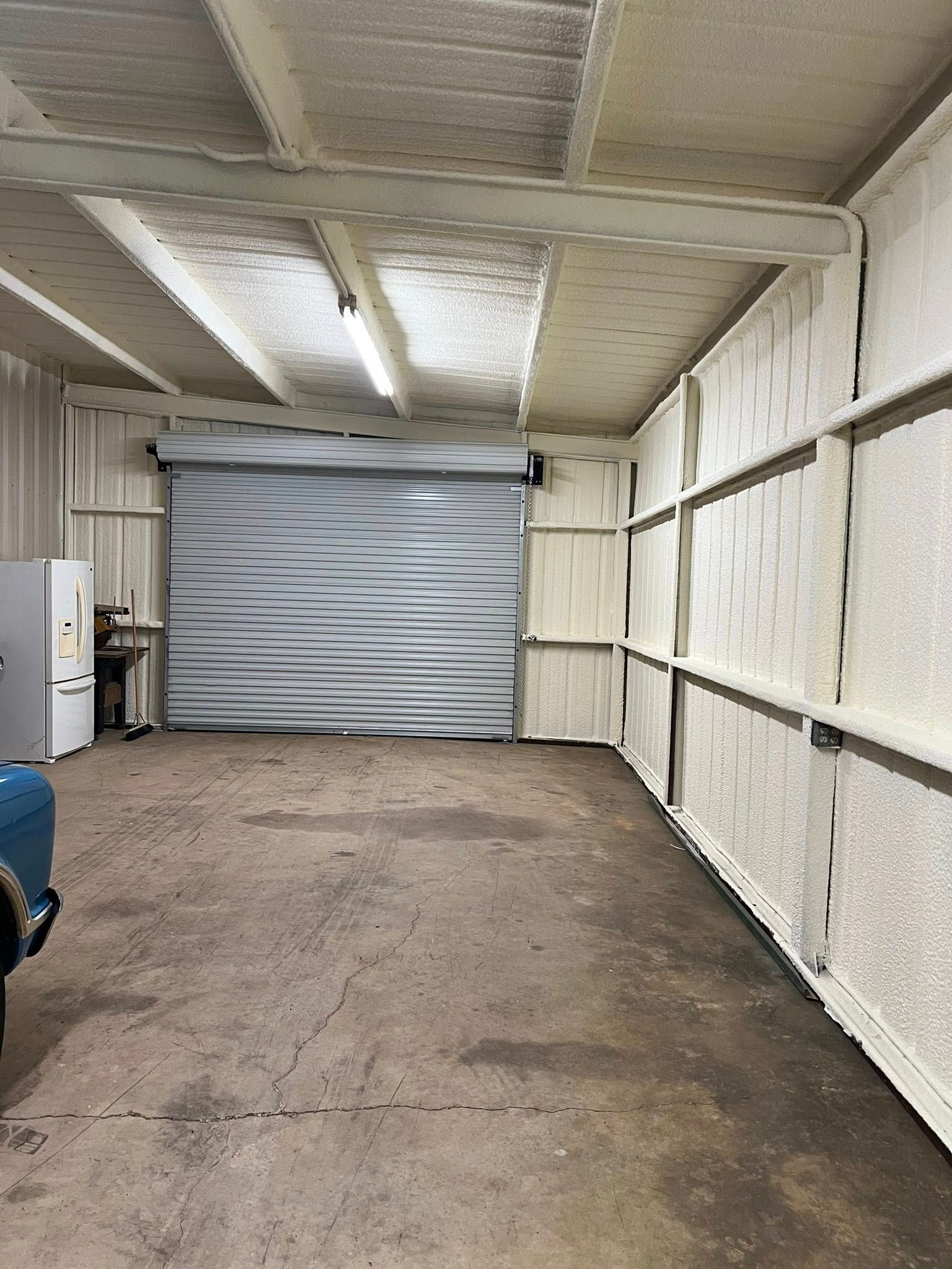 Garage interior with spray foam insulation on walls and ceiling, closed garage door.