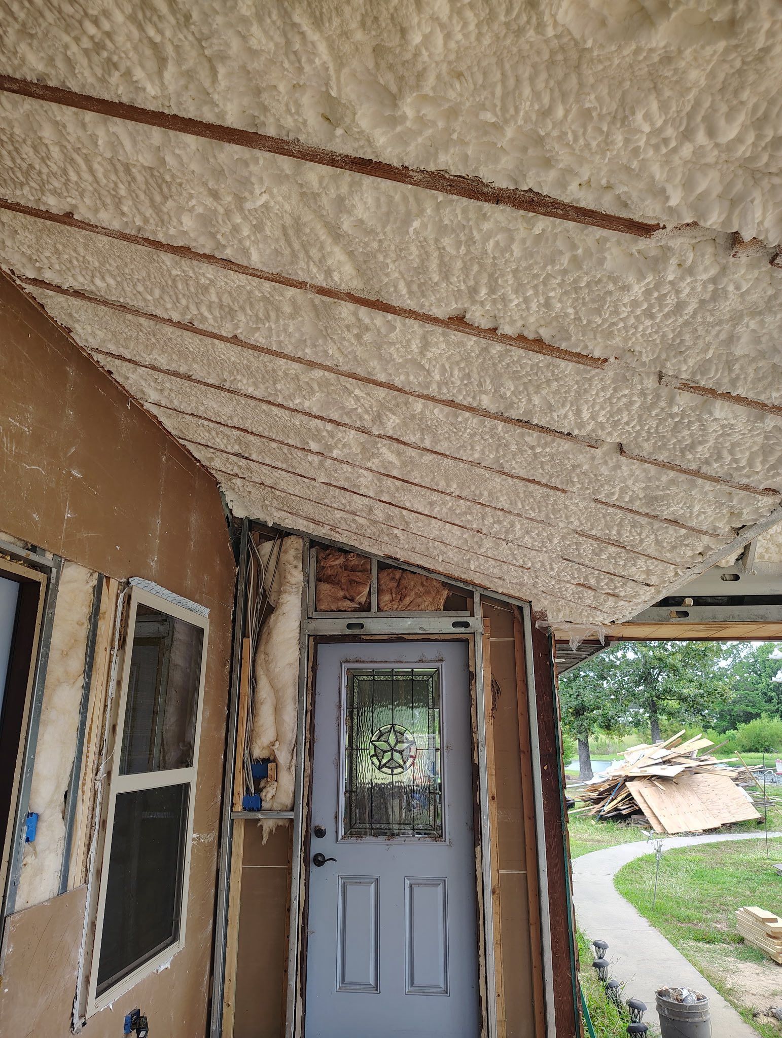 View of a porch ceiling with spray foam insulation. A door is in the center with a walkway leading to a backyard.