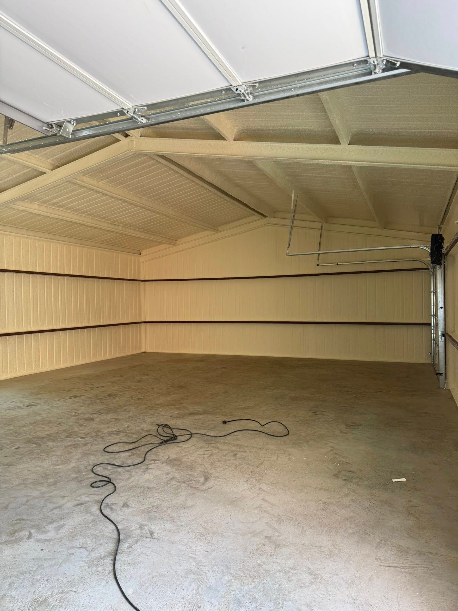 Interior of a tan garage with concrete floor, black cord, and overhead garage door track.