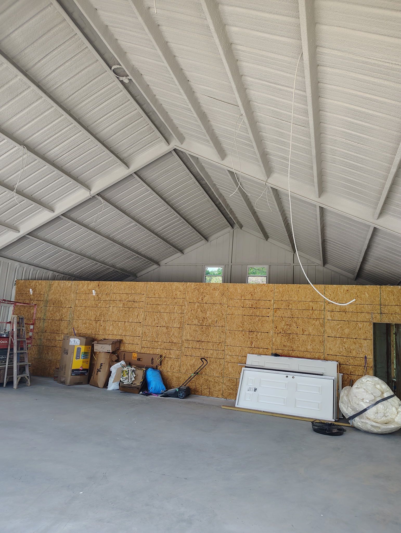 Interior view of a building with a high, white-painted ceiling and a wood-paneled wall, containing various items.