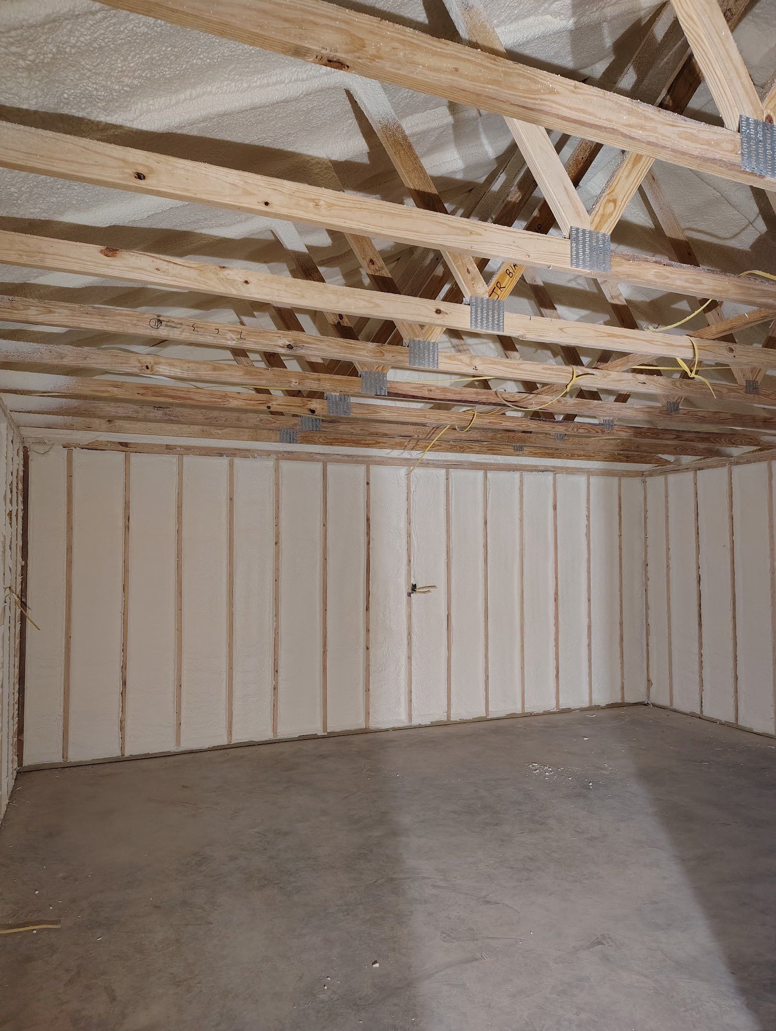 Interior of a room with exposed wooden rafters, concrete floor, and insulation panels on the walls.
