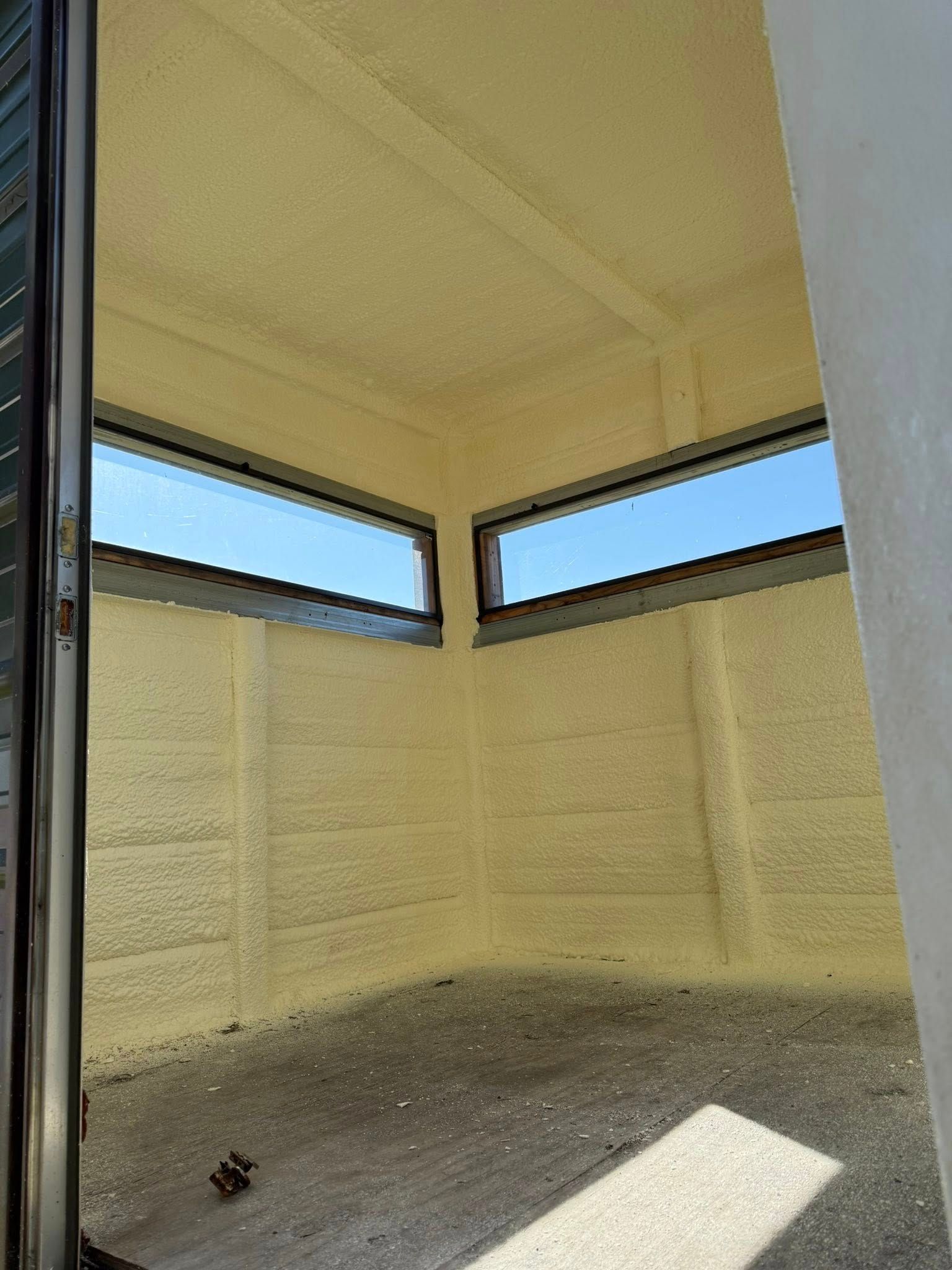Interior view of a small room with spray foam insulation. Two windows show blue sky.
