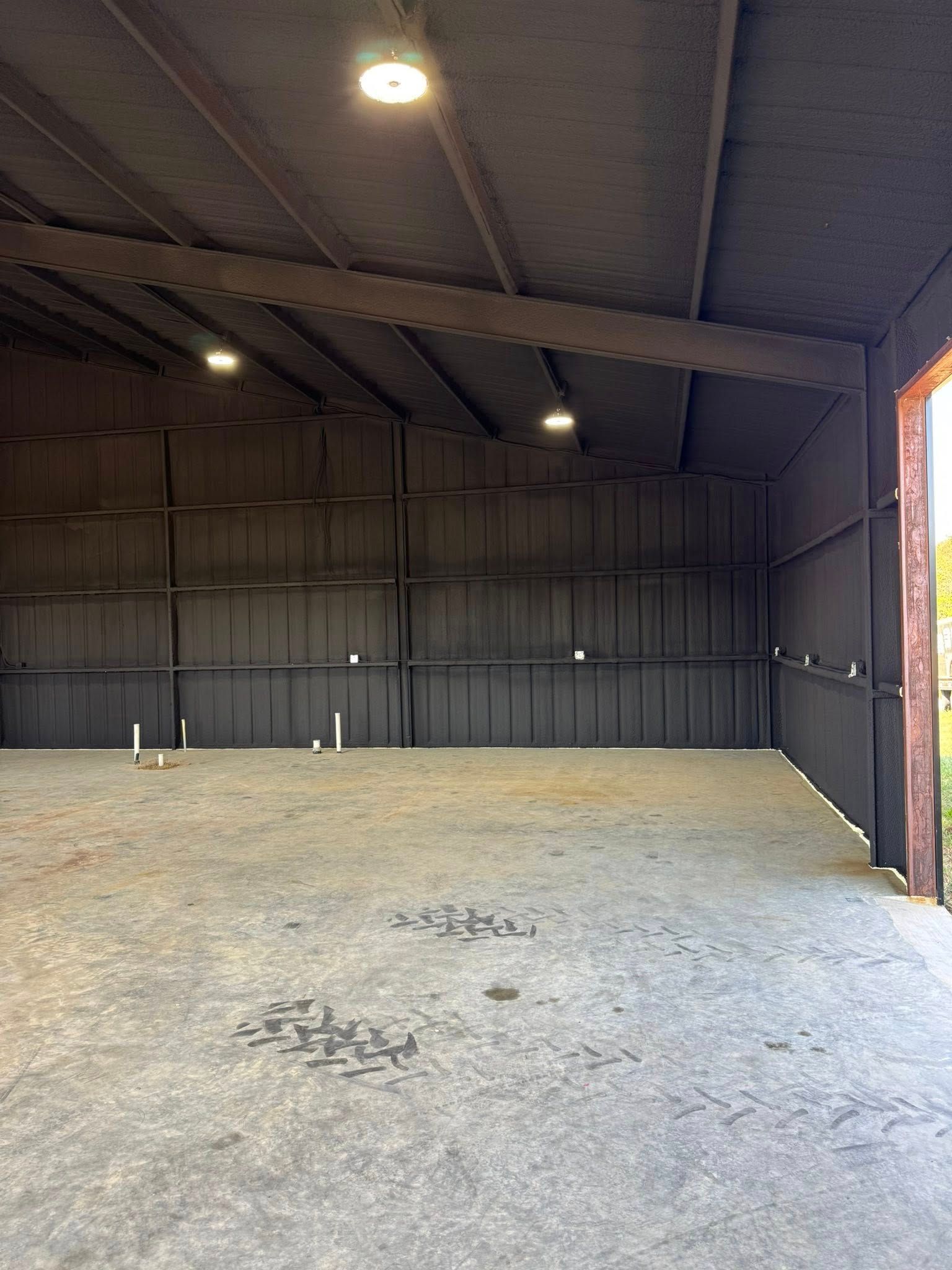 Empty metal-framed building interior with a concrete floor, dark walls, and ceiling lights.