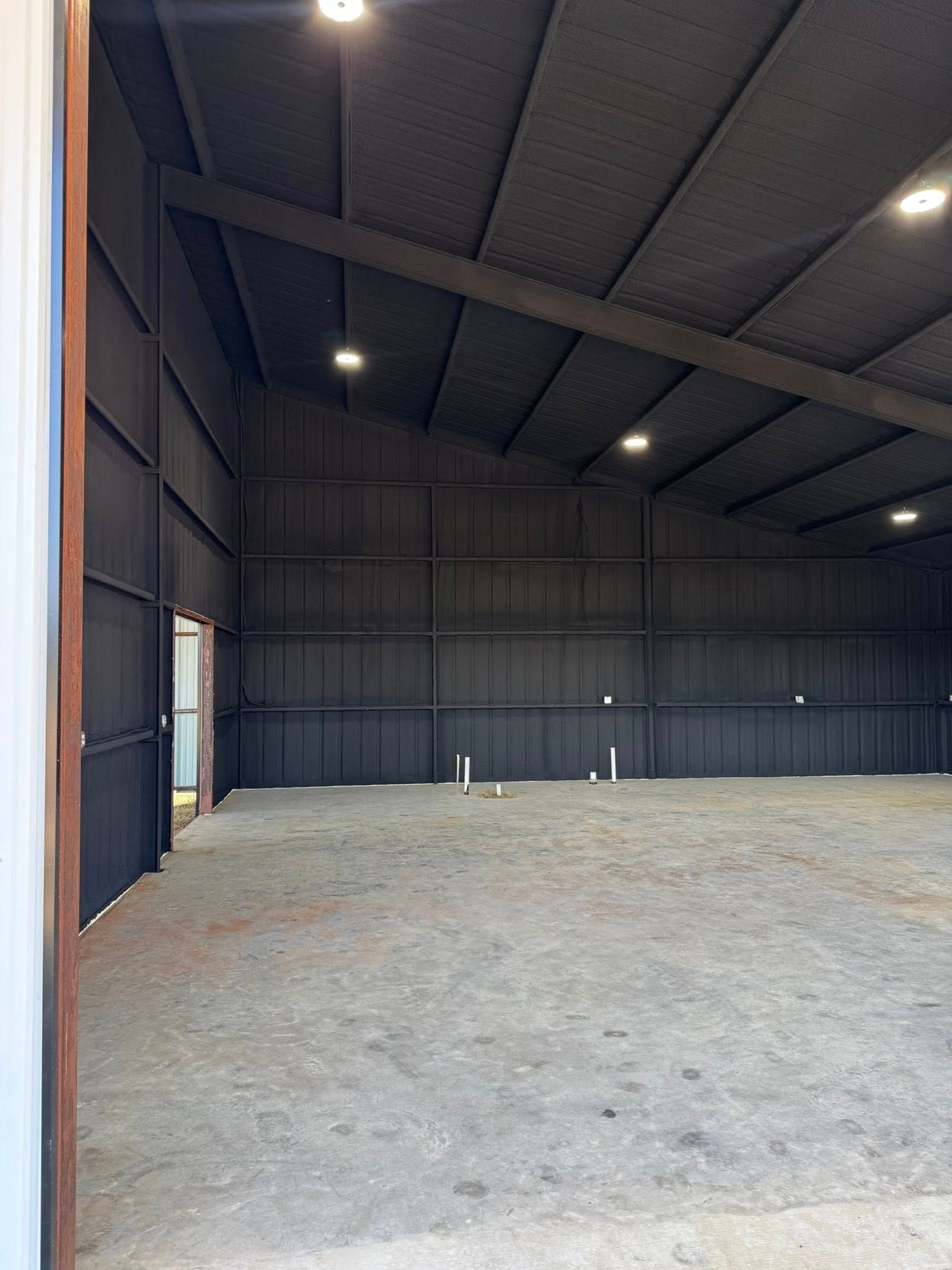 Inside of a large, empty metal building with a dark gray interior and overhead lights.