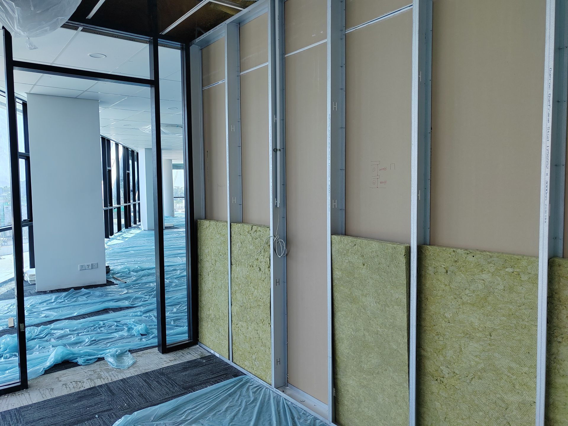 Interior view of a construction site. Metal studs, insulation, and drywall are installed. Broken glass on the floor.