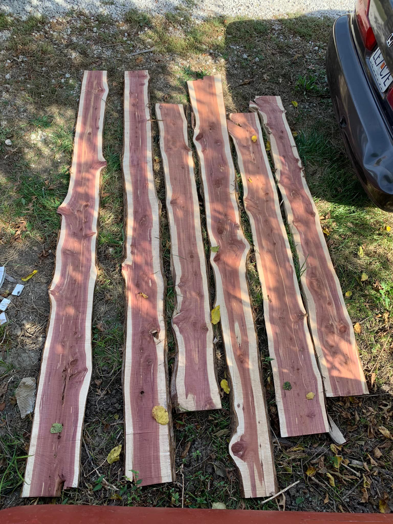 Seven reddish-brown cedar planks with live edges, lying on a surface with scattered leaves.