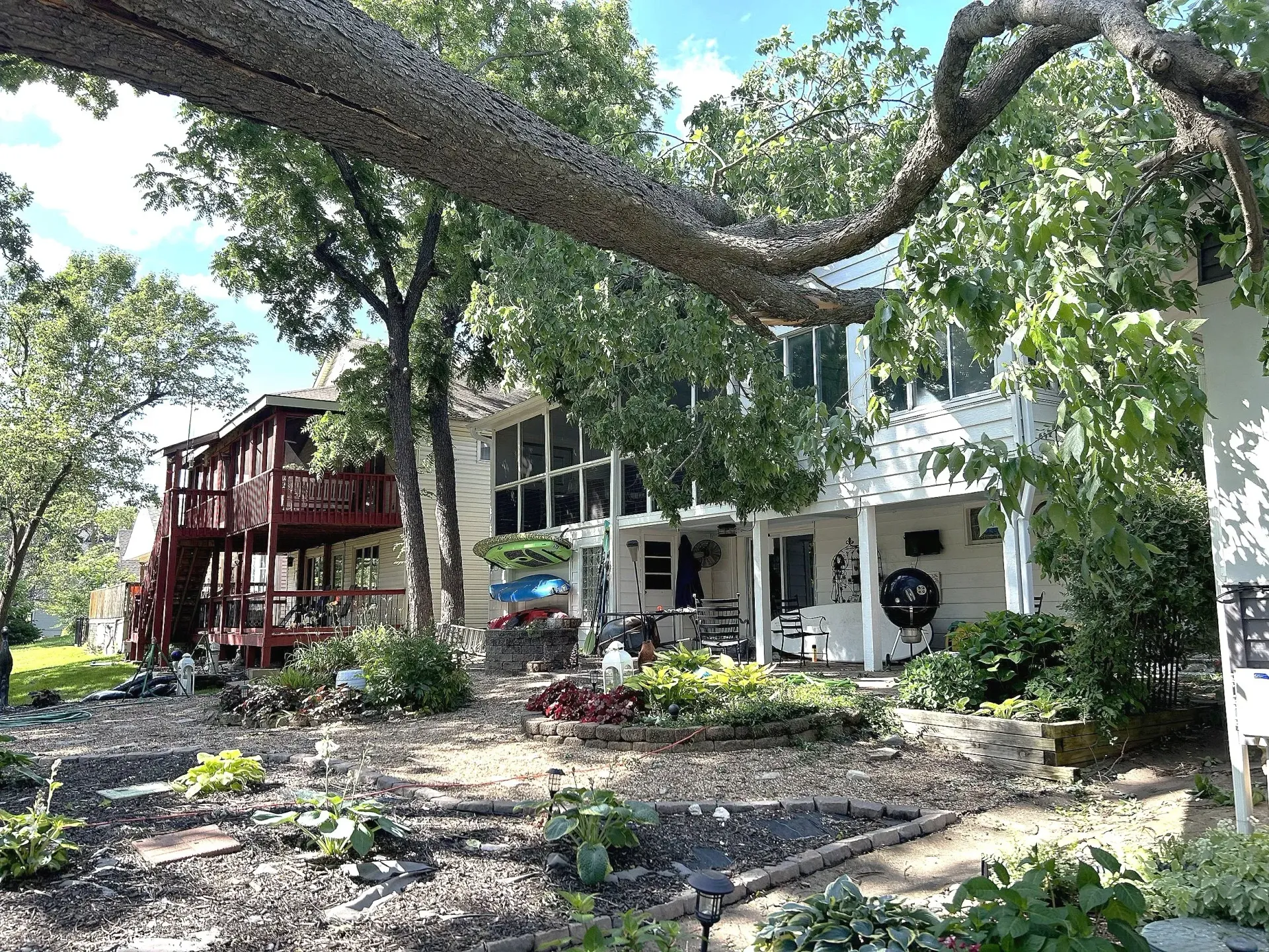 A white house with a red balcony, surrounded by trees and a garden on a sunny day.