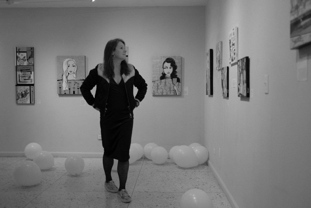 A woman is standing in a room with balloons and paintings on the wall.