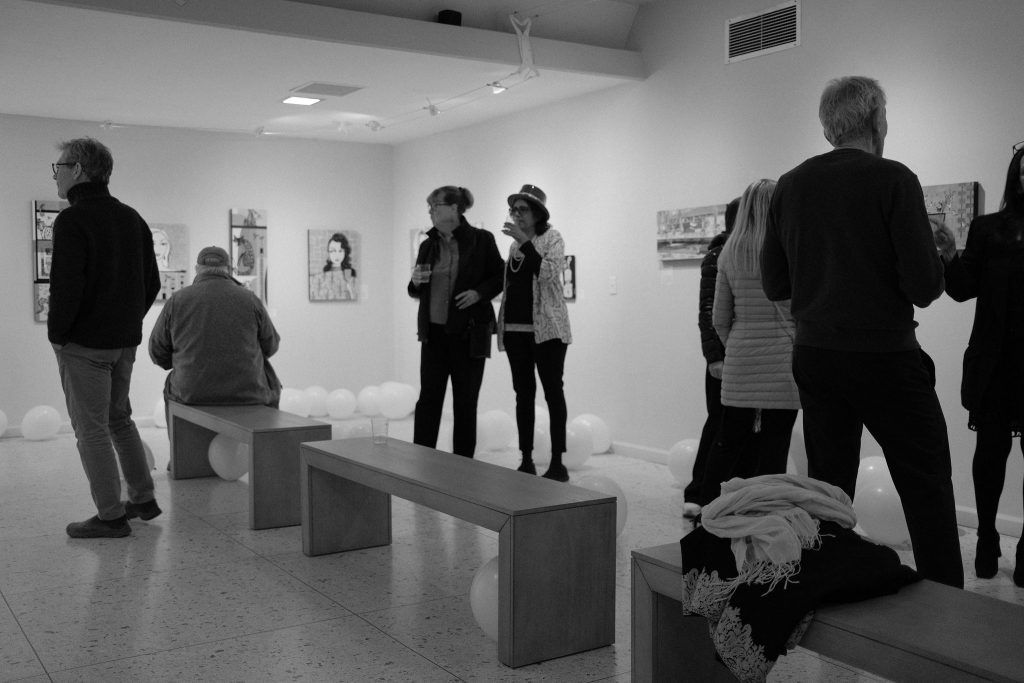 A group of people are standing in a museum looking at paintings.