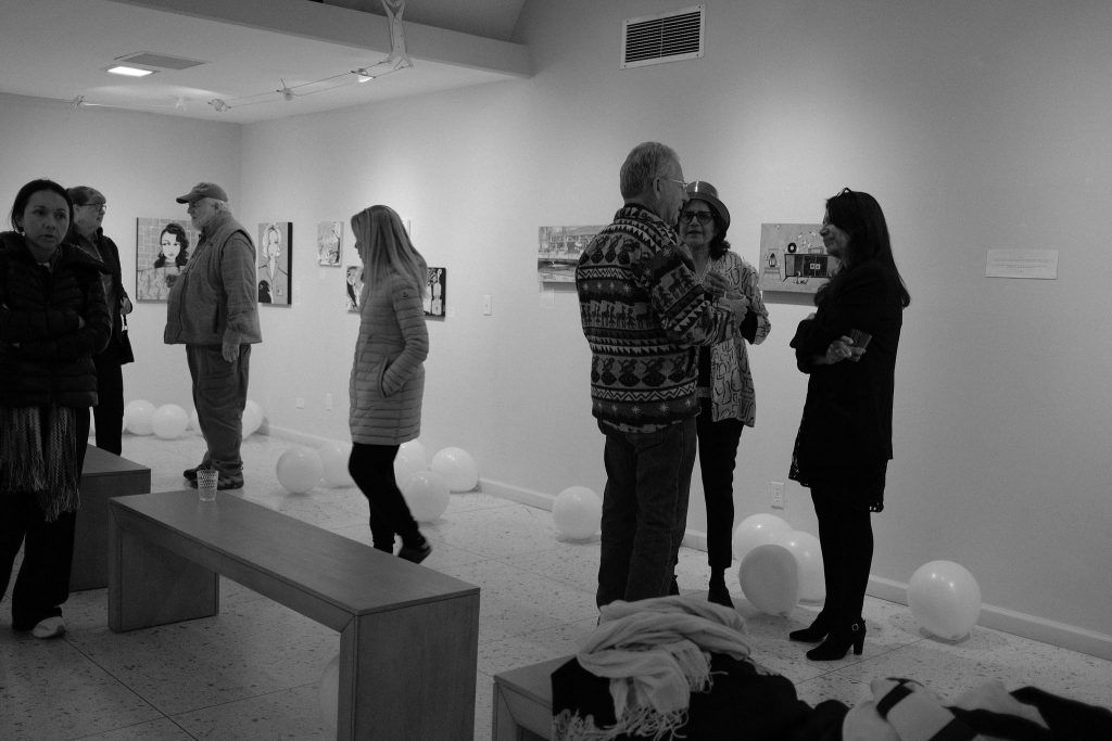 A group of people are standing in a room looking at paintings.