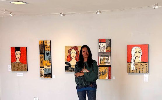 A woman is standing in front of a wall with paintings on it.