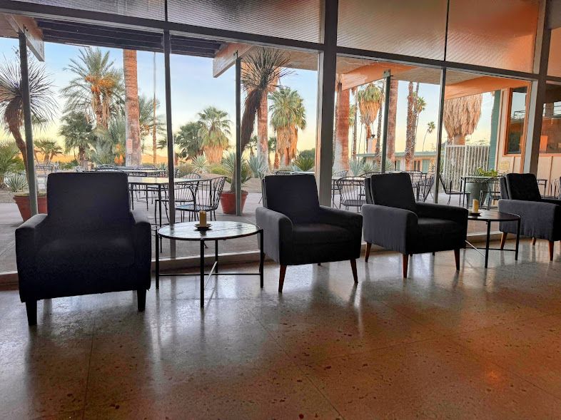 A row of chairs and tables in a room with palm trees in the background.