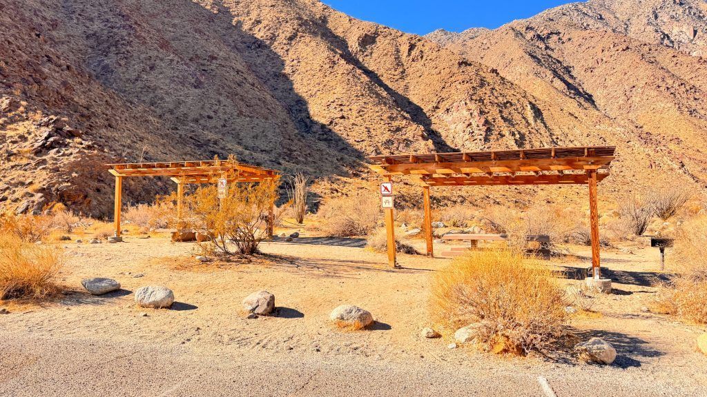 A group of wooden structures in the desert with mountains in the background.