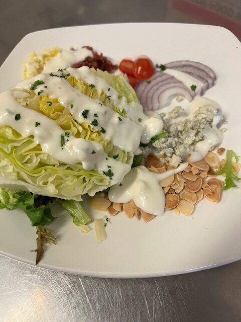 A salad with lettuce tomatoes onions and blue cheese dressing on a white plate