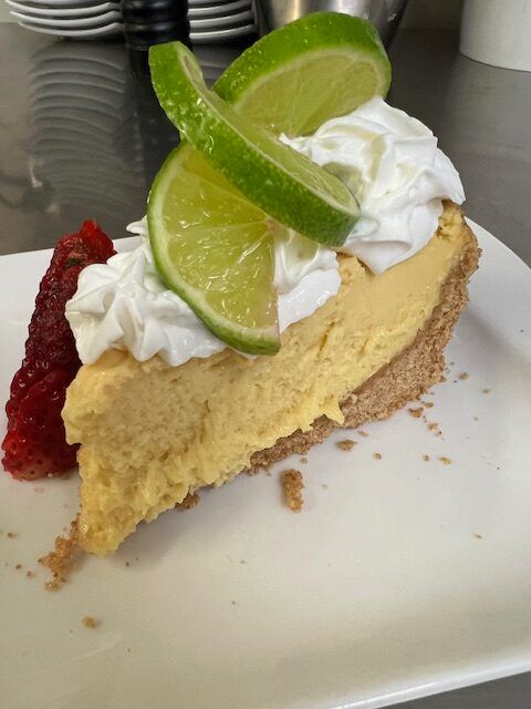 A slice of key lime pie with whipped cream and lime slices