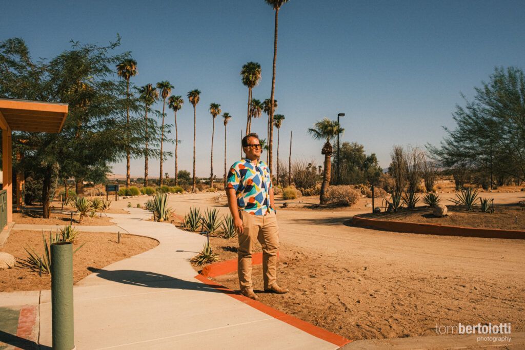 A man is standing on a sidewalk in a park with palm trees in the background.