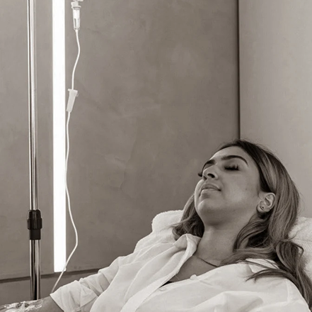 Woman receiving IV drip in a medical setting, eyes closed