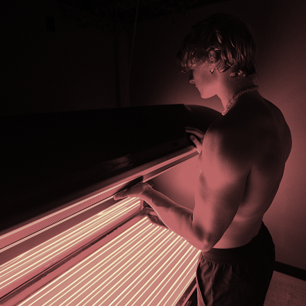 A shirtless man is standing in front of a tanning bed