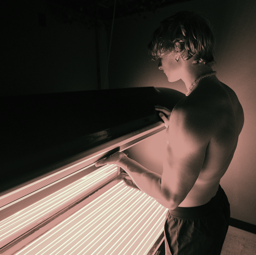 A shirtless man is standing in front of a tanning bed
