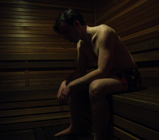 A shirtless man is sitting in a wooden sauna.