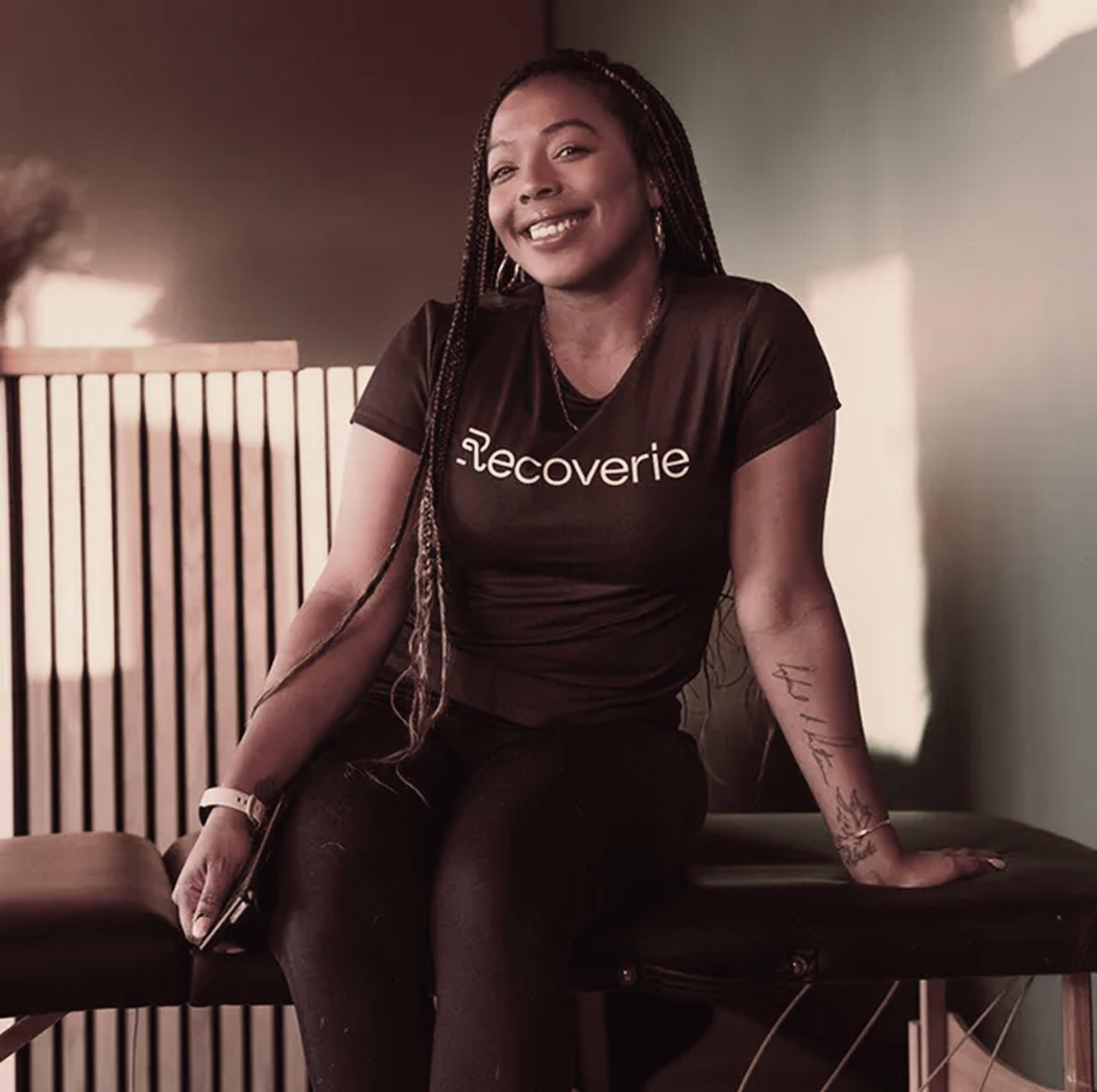 A woman wearing a black recovery shirt sits on a table