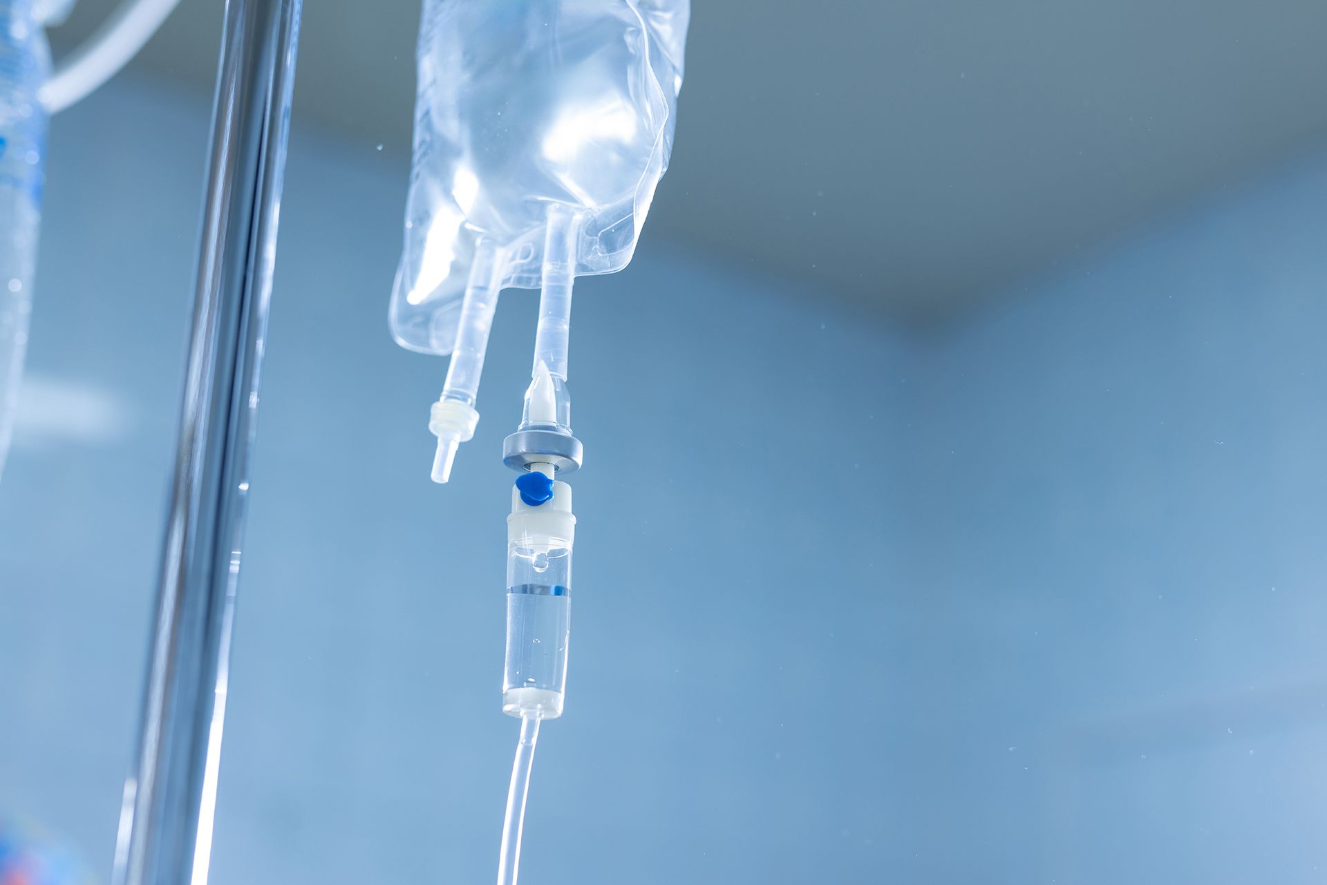 A clear intravenous fluid bag hanging on a stand, with a drip chamber showing liquid flowing through the tubing.