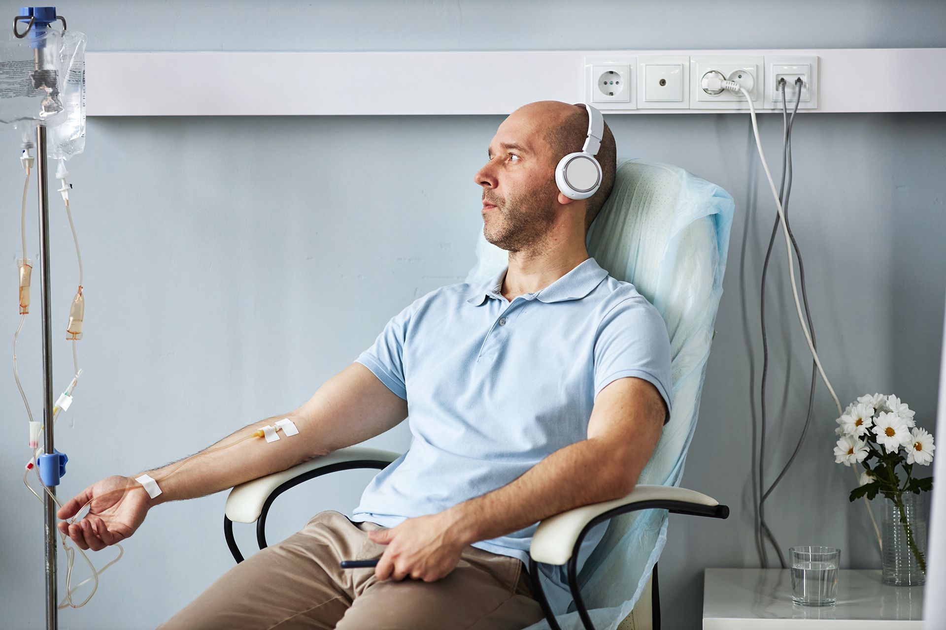 Patient reclining in a clinic chair with IV drip, wearing headphones and listening to music.