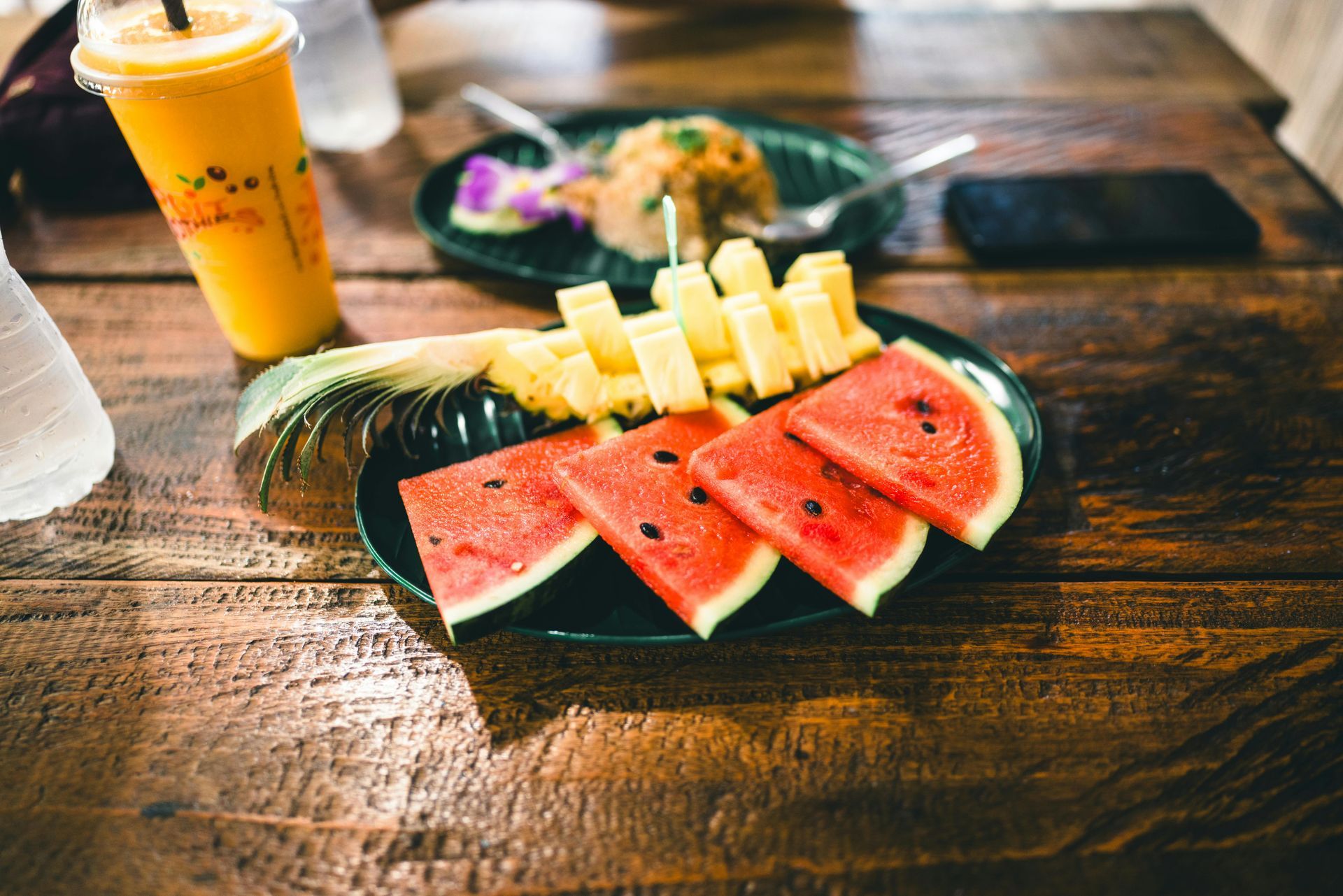Watermelon, pineapple, and drink on a wooden table.