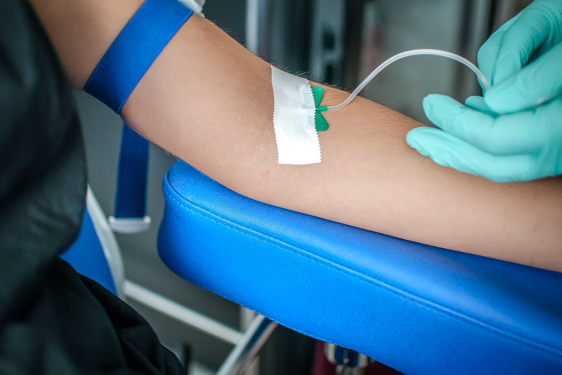 A gloved healthcare professional inserting a needle for a blood draw into a patient's arm at a clinic.