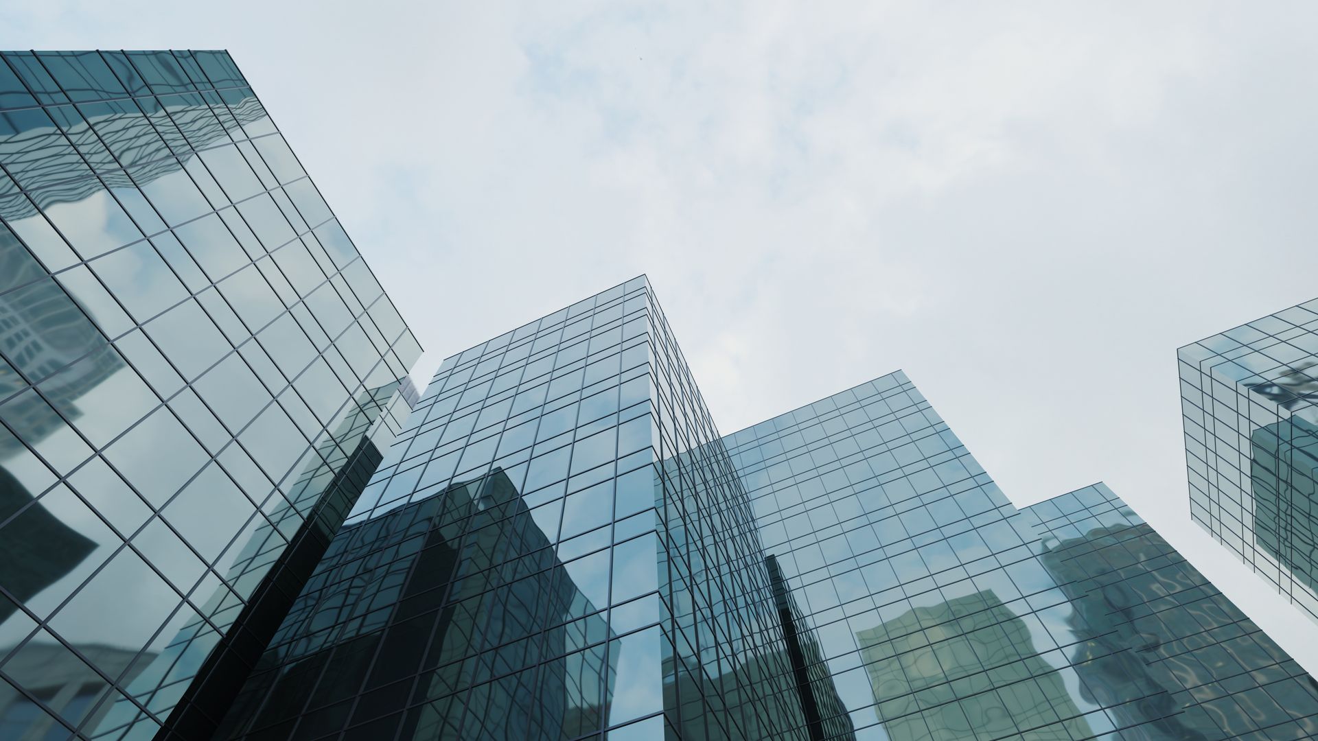 Looking up at a group of tall buildings with a cloudy sky in the background.