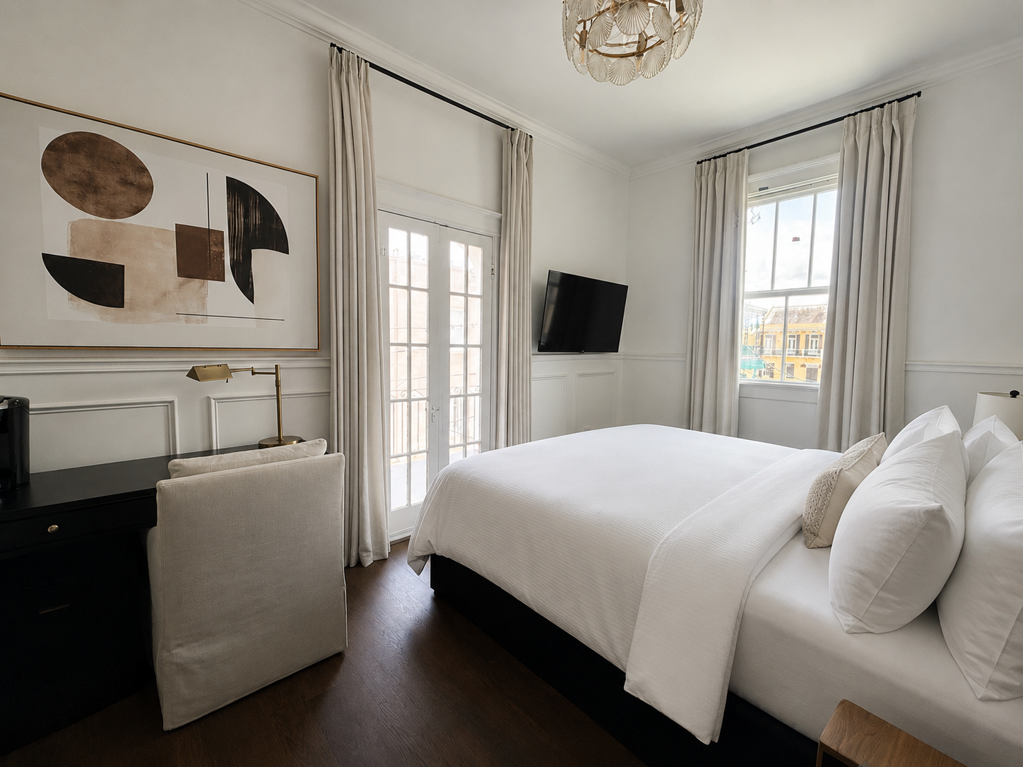 Bright bedroom with a white bed, tall windows, wall art, and a wall-mounted TV.